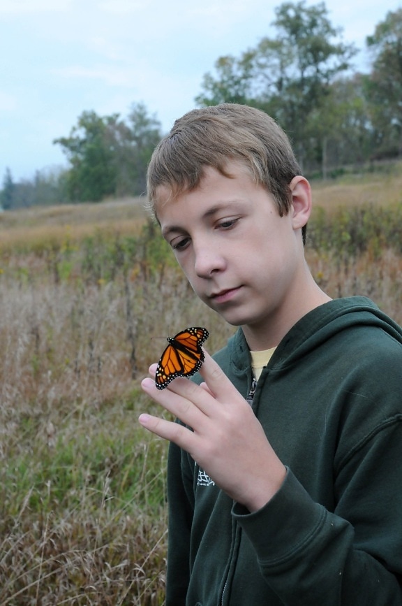 young male, holds, Monarch, butterfly, insect, finger