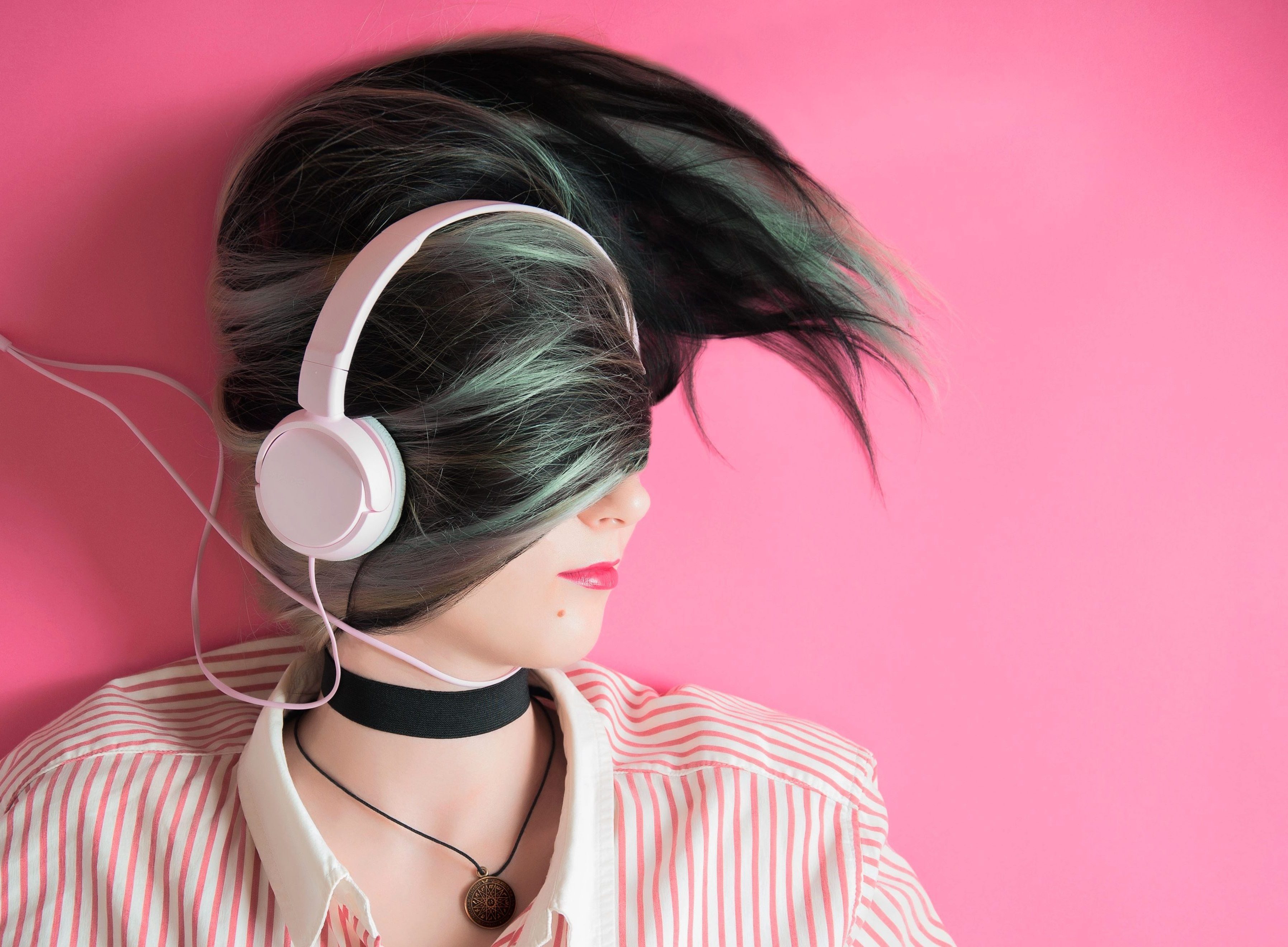Menina ouvindo música em fones de ouvido na parede rosa. garota
