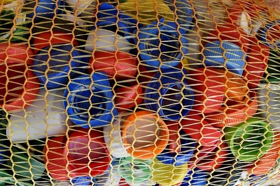 Lähikuva värikkäistä muovipullojen kansista verkkojätesäkissä