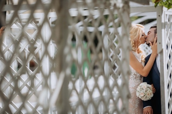 bride, groom, kiss, alone, private, hiding, embrace, affection, wedding, fence