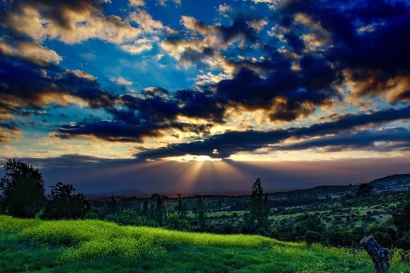 Awan biru tua di cakrawala saat senja dengan panorama padang rumput dan lapangan pedesaan dengan rumput