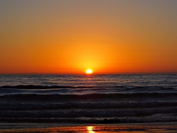 Solnedgang på havhorisonten med vann med bølger i skumringen
