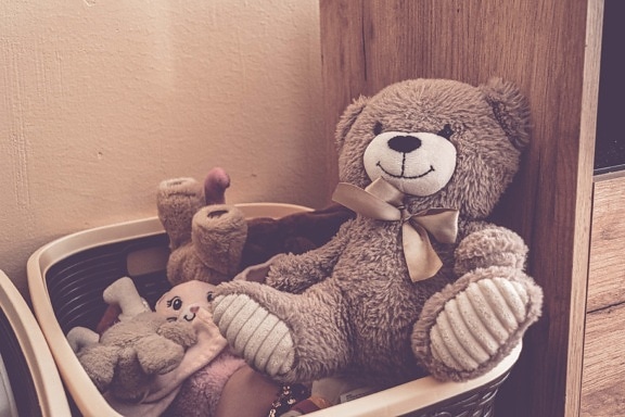 Plush teddy bear toy in wicker basket box with other toys in room