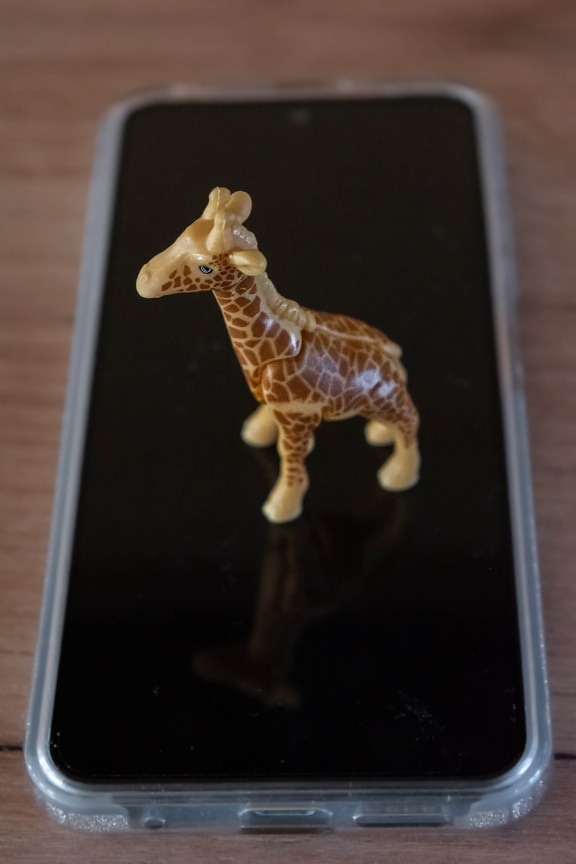 Close-up of miniature plastic giraffe toy on mobile phone