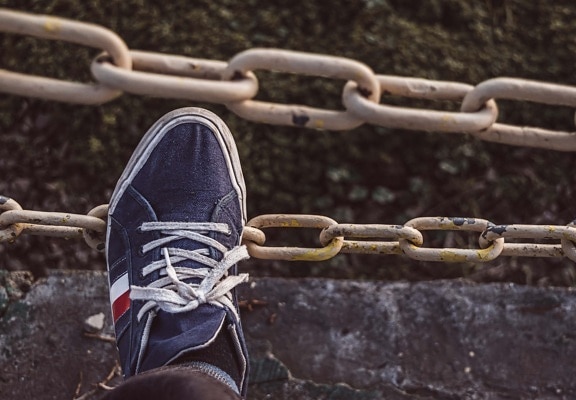 Leg with old fashioned dark blue sneakers and white shoelace on old metal chain