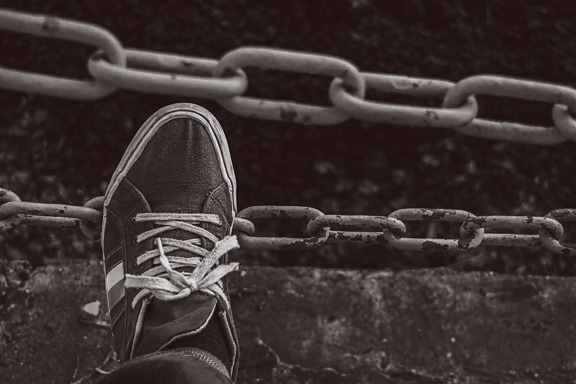 Foot in old fashioned sneakers on cast iron chain black and white photo