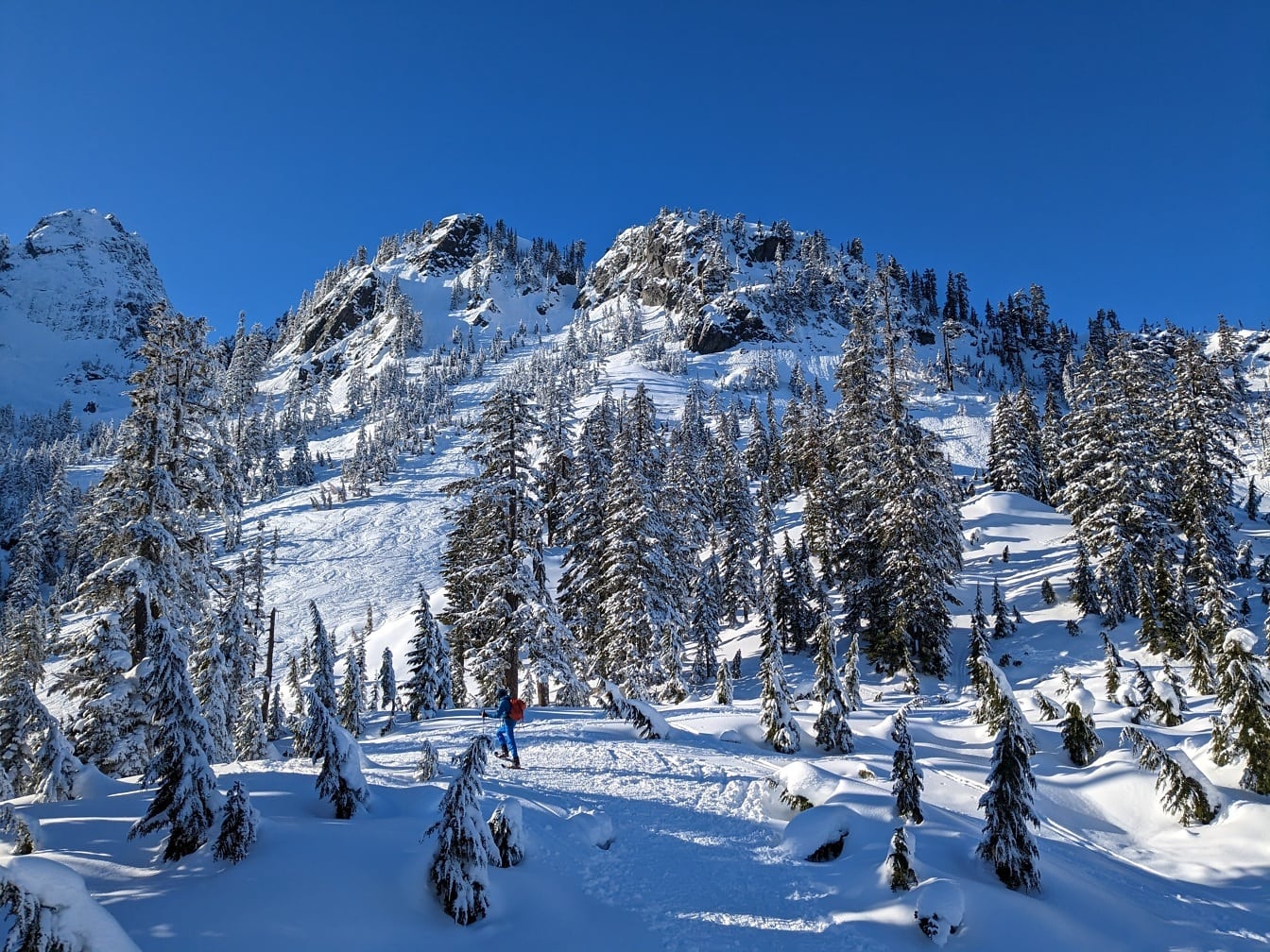 Esquiador escalando em montanhas nevadas em dia brilhante
