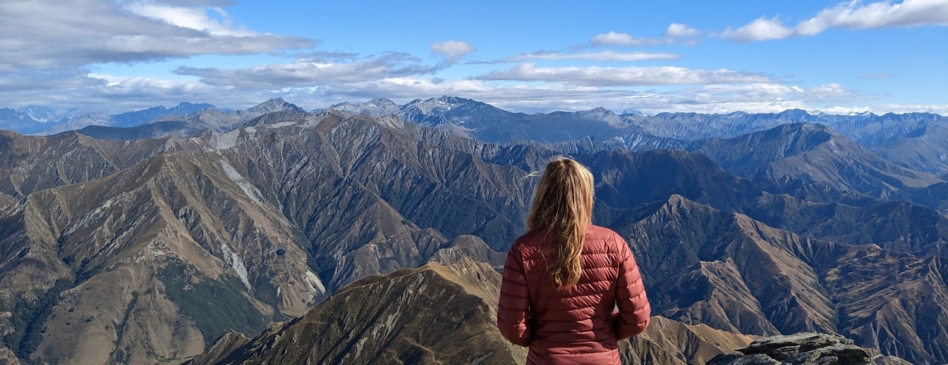 Giovane donna bionda in giacca rossa al picco della montagna