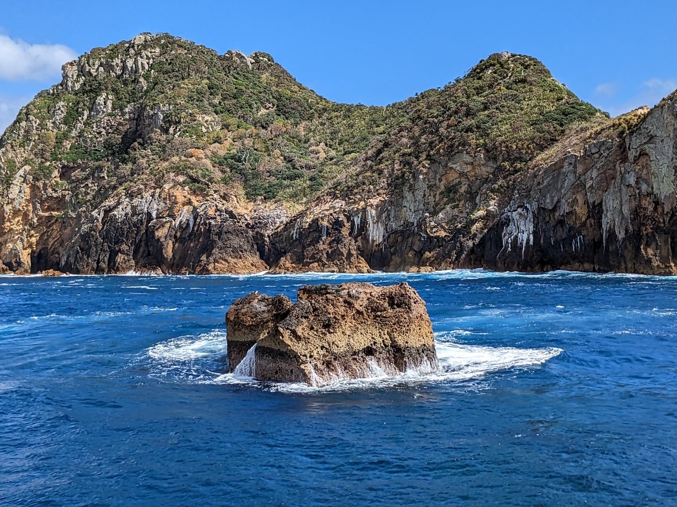 海浪飞溅到新西兰岩石海岸线上的小岛上