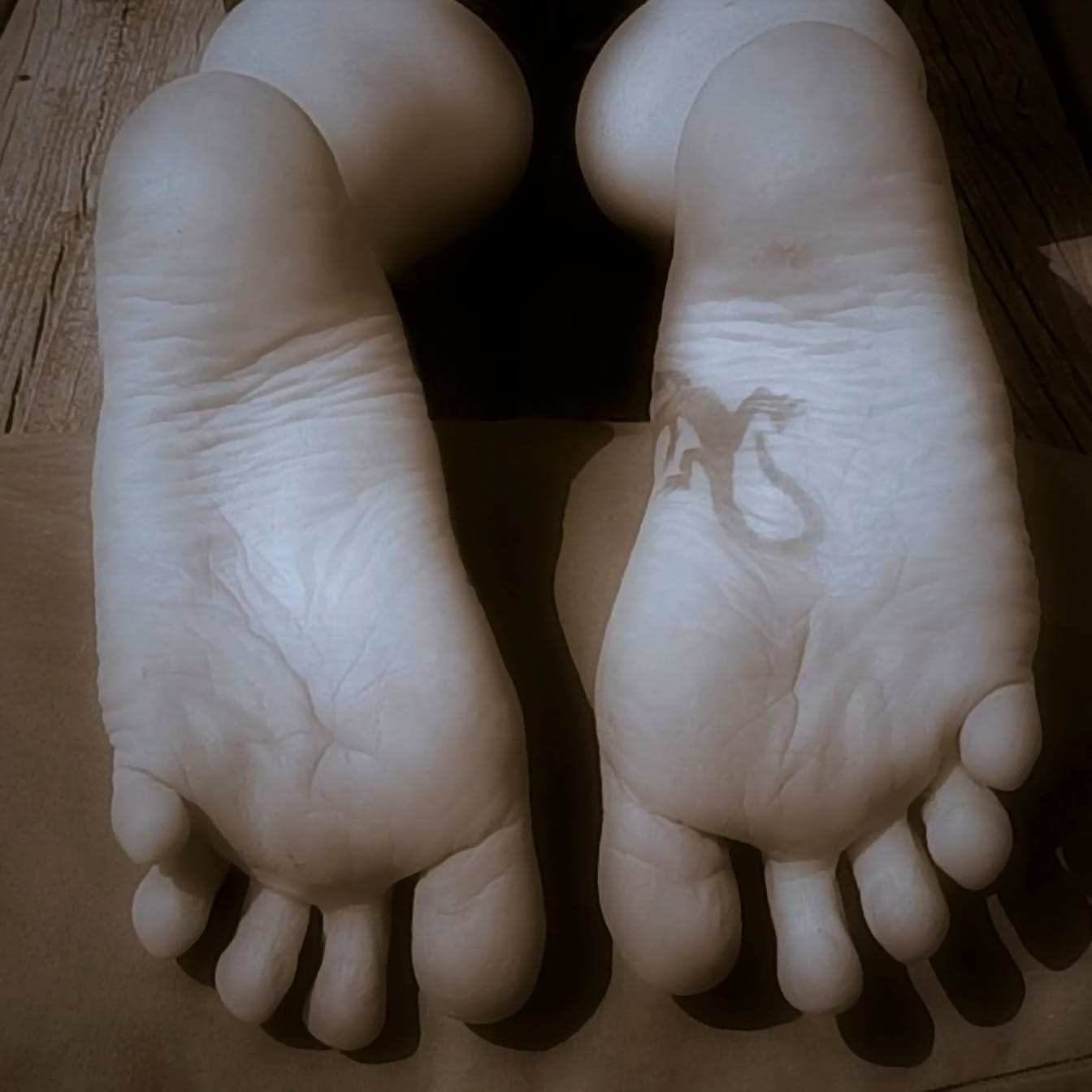 Detail tetování na bosých nohou – sépiová fotografie
