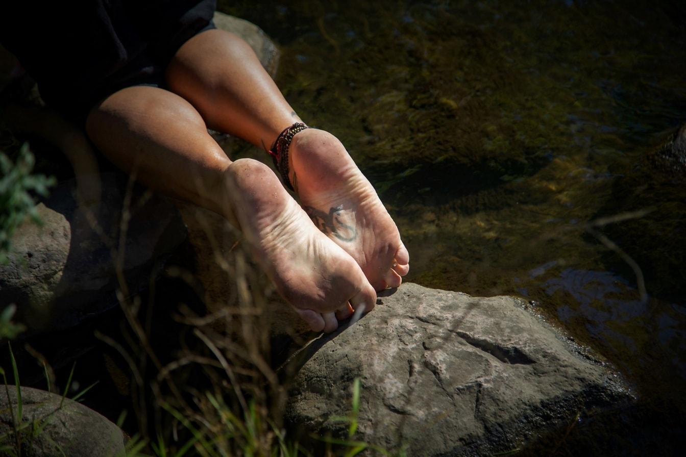 Die nackten Füße eines Mannes auf einem großen Stein in einem felsigen Fluss