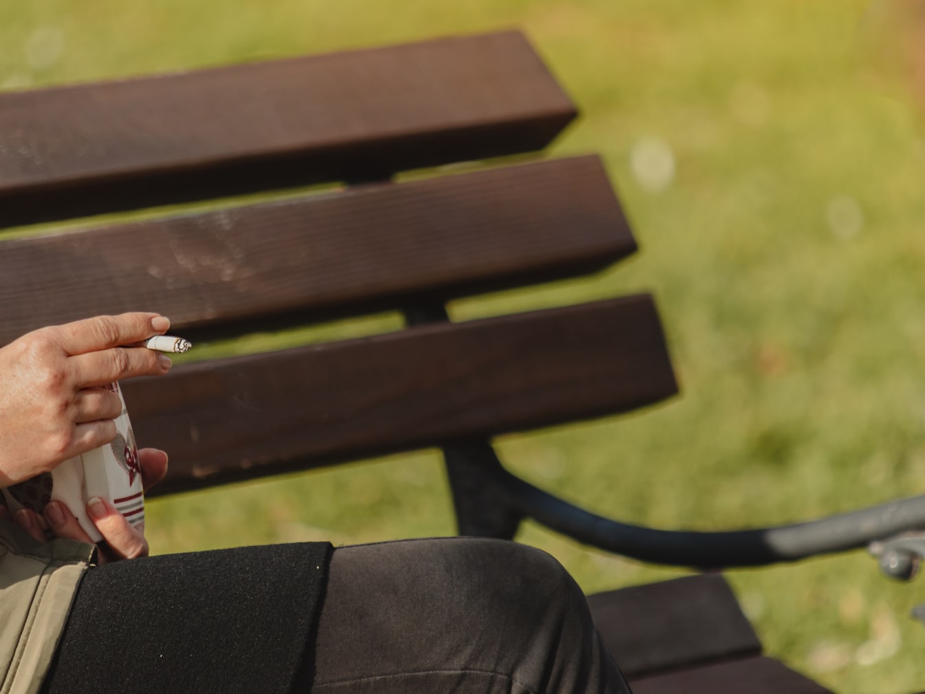 Osoba sedící a držící hrnek a cigaretu v rukou