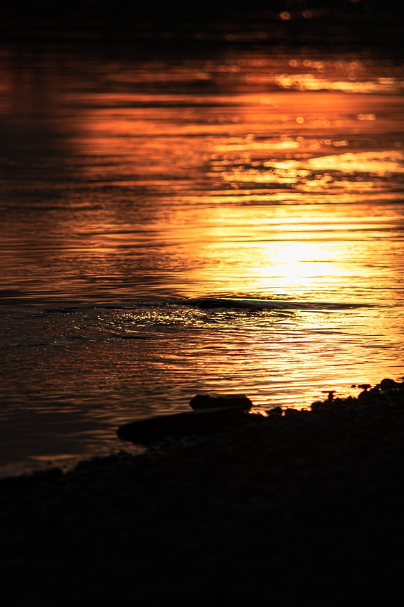 Water ripple on water level horizon at orange yellow sunrise