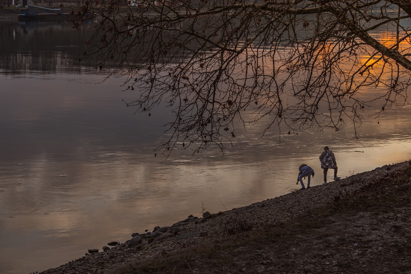Silueta osob na břehu řeky při západu slunce