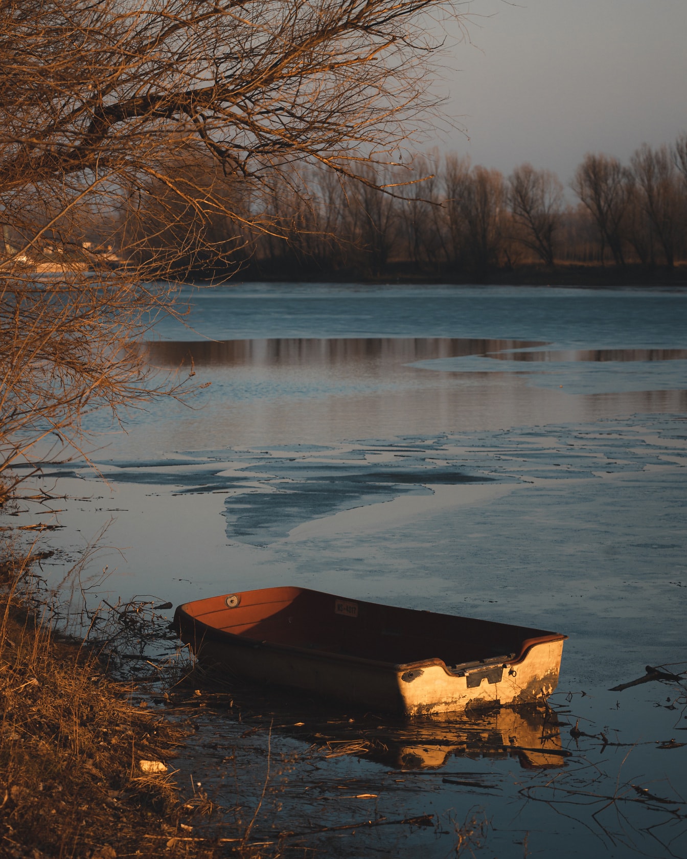 Barcă veche de plastic pe malul lacului înghețat