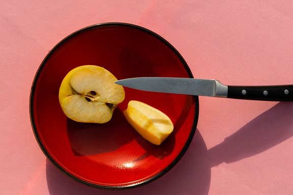 Yellow apple slices in dark red bowl with knife