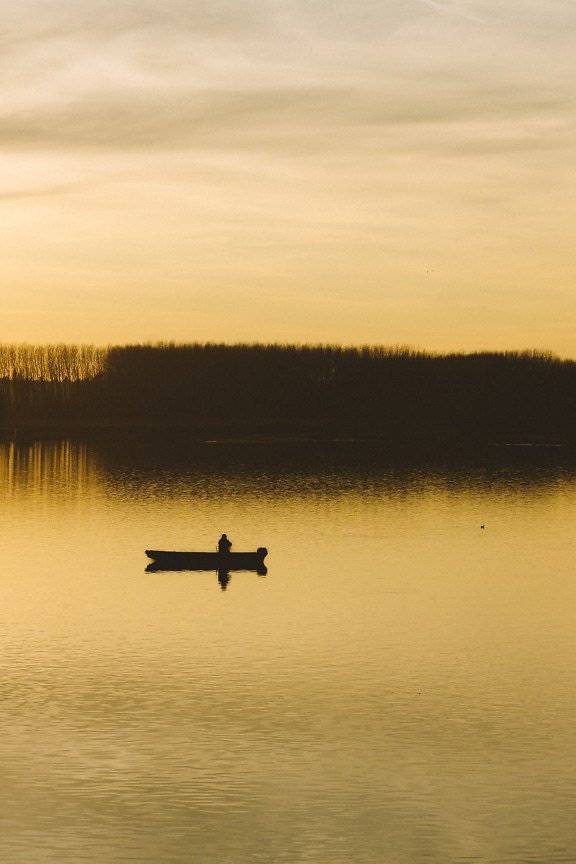Silhouette of fishing boat on lakeside in dusk
