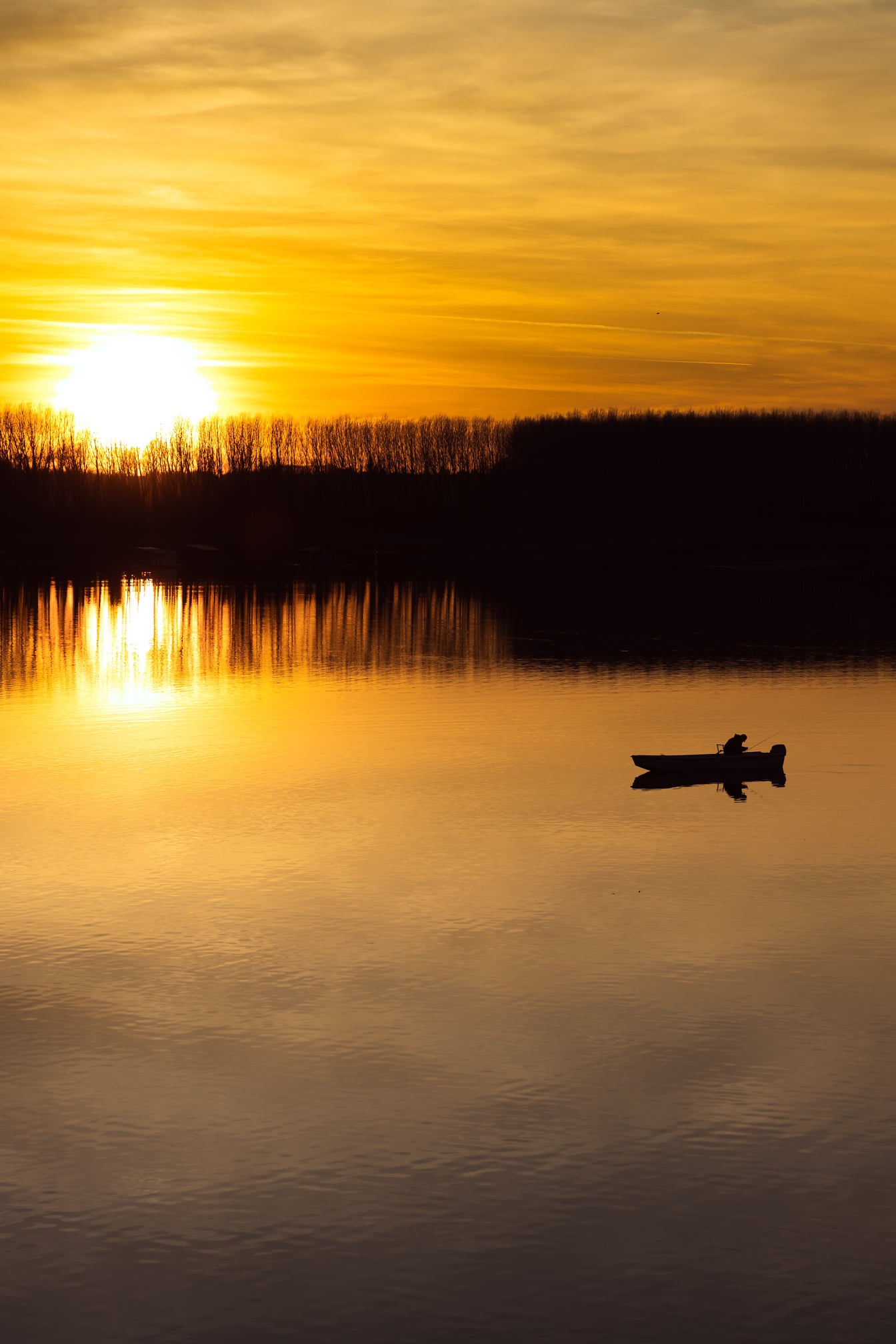 พระอาทิตย์ขึ้นสดใสเหนือริมทะเลสาบพร้อมเงาของเรือประมง