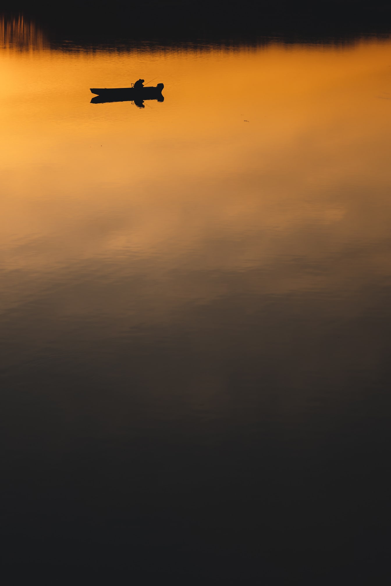 Silhuete rybára v rybárskej lodi na pokojnej vode pri východe slnka