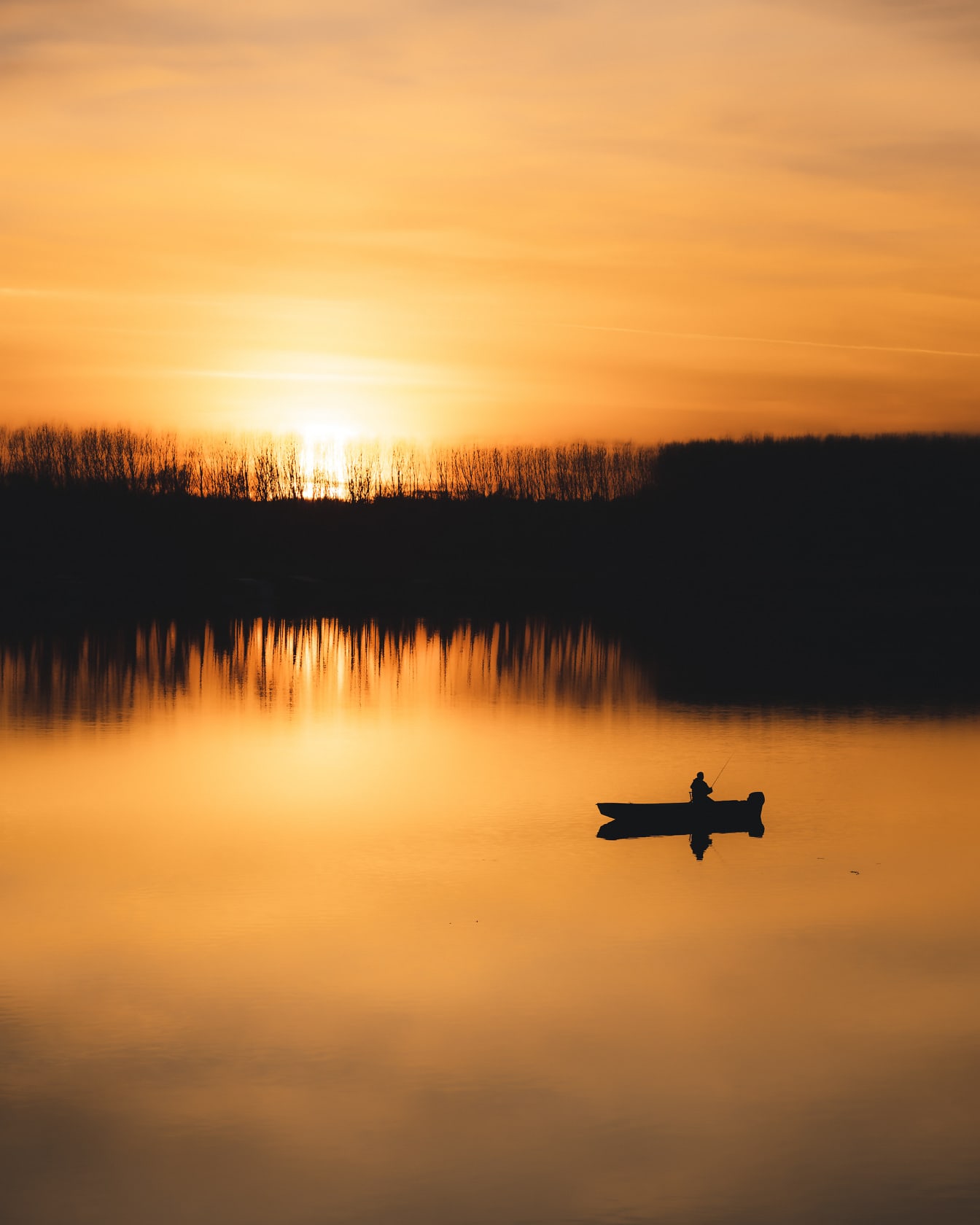 Oranžovo žltý západ slnka na brehu rieky so siluetou rybárskej lode