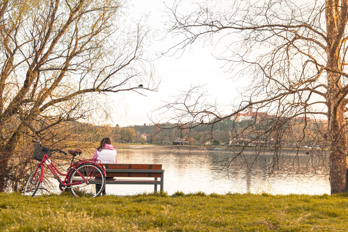 Жена седи на пейка край брега на реката през есенния сезон