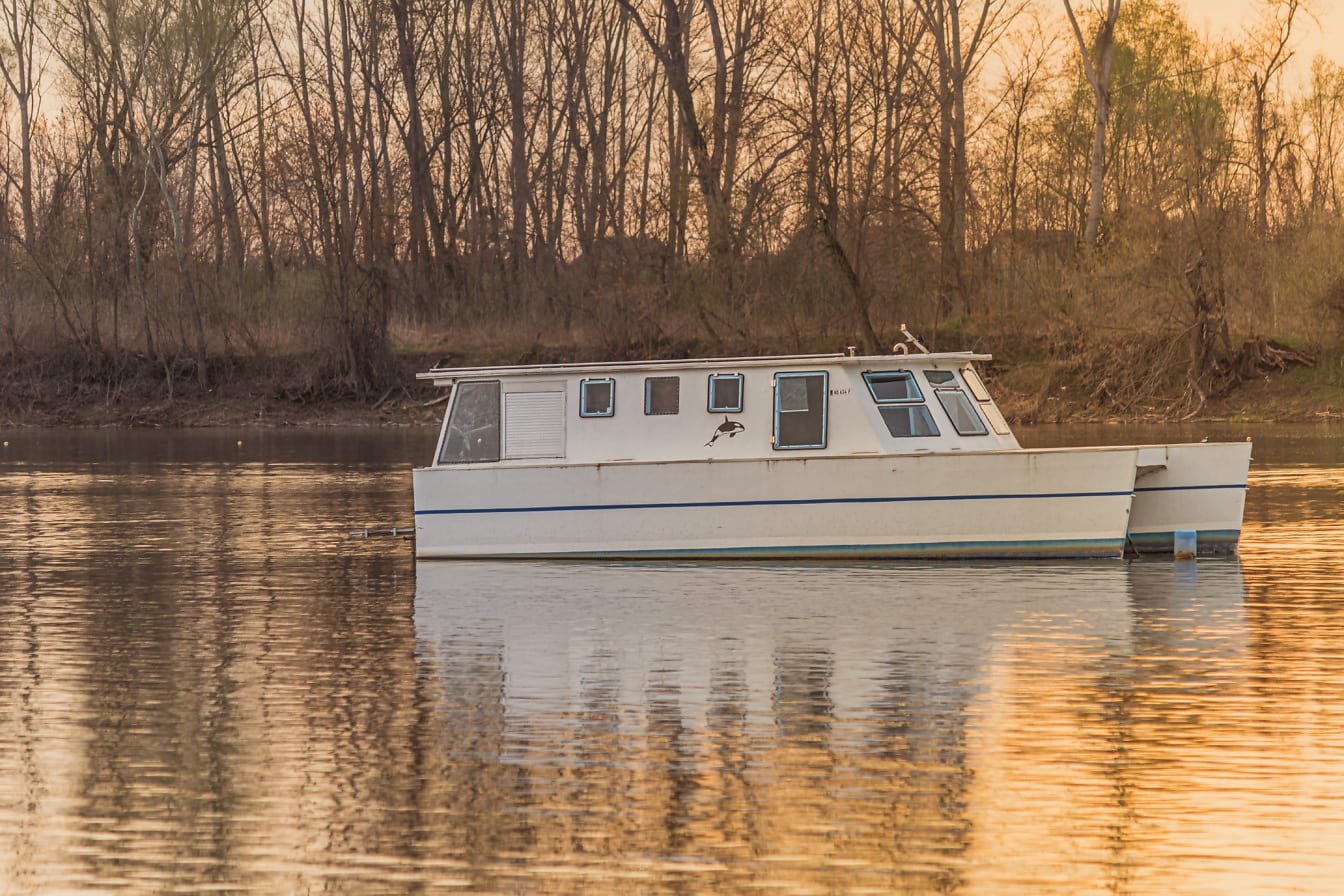 Malá bílá jachta na klidné řece při východu slunce