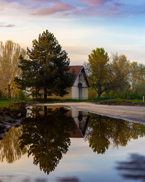 Countryside house reflection in pond on dirt road