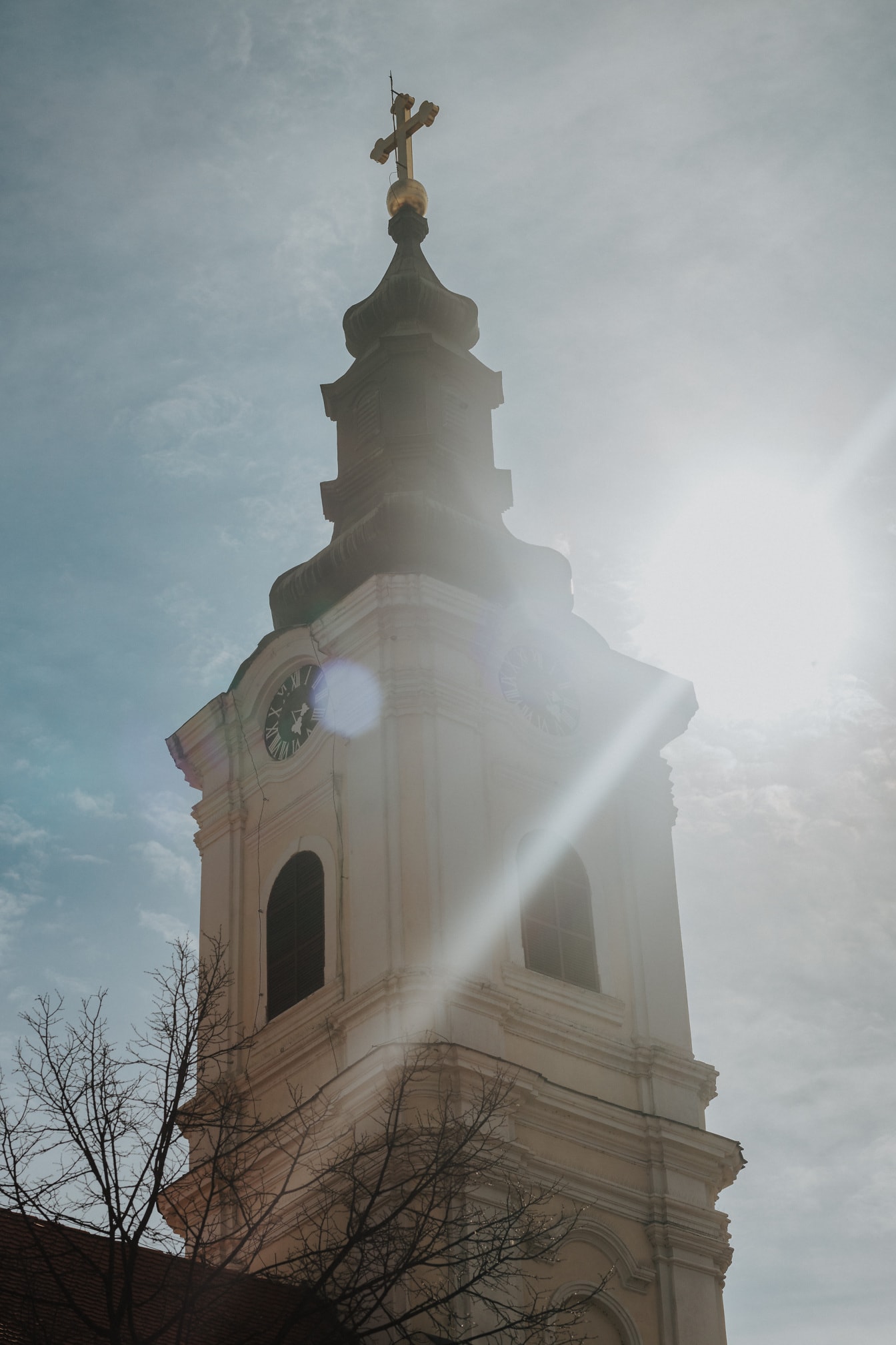 Križ zlatnog sjaja na crkvenom tornju sa svijetlim sunčevim zrakama