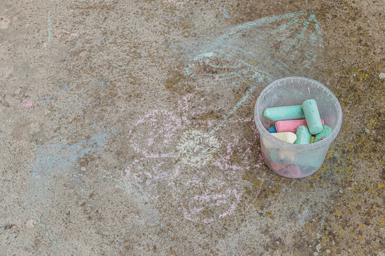 Colorful drawing chalk in transparent plastic bucket o concret