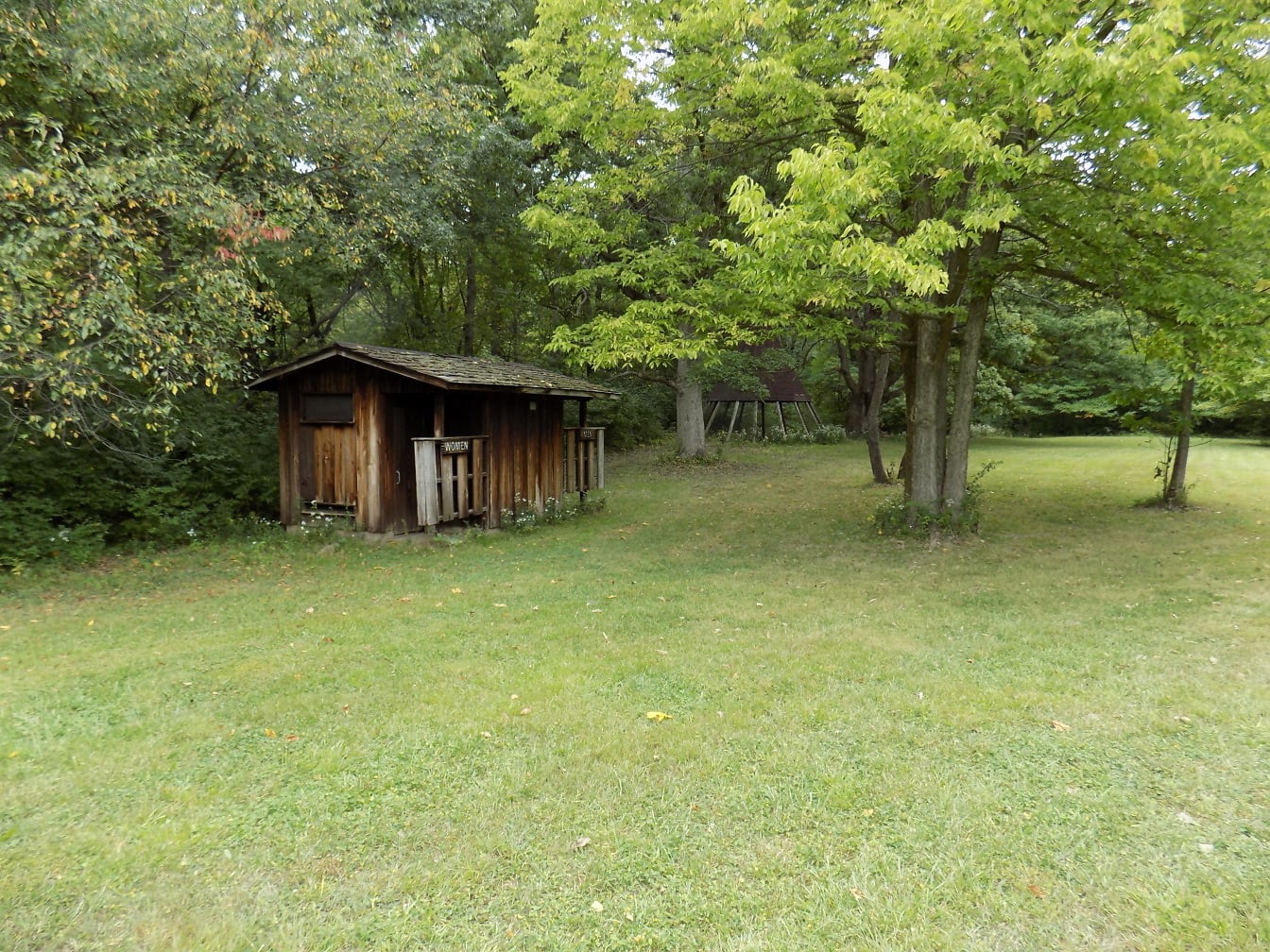 Drewniana toaleta w stodole w starym stylu na podwórku z zielonym trawnikiem