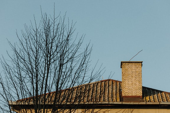 Chimney on house rooftop covered with roof tiles