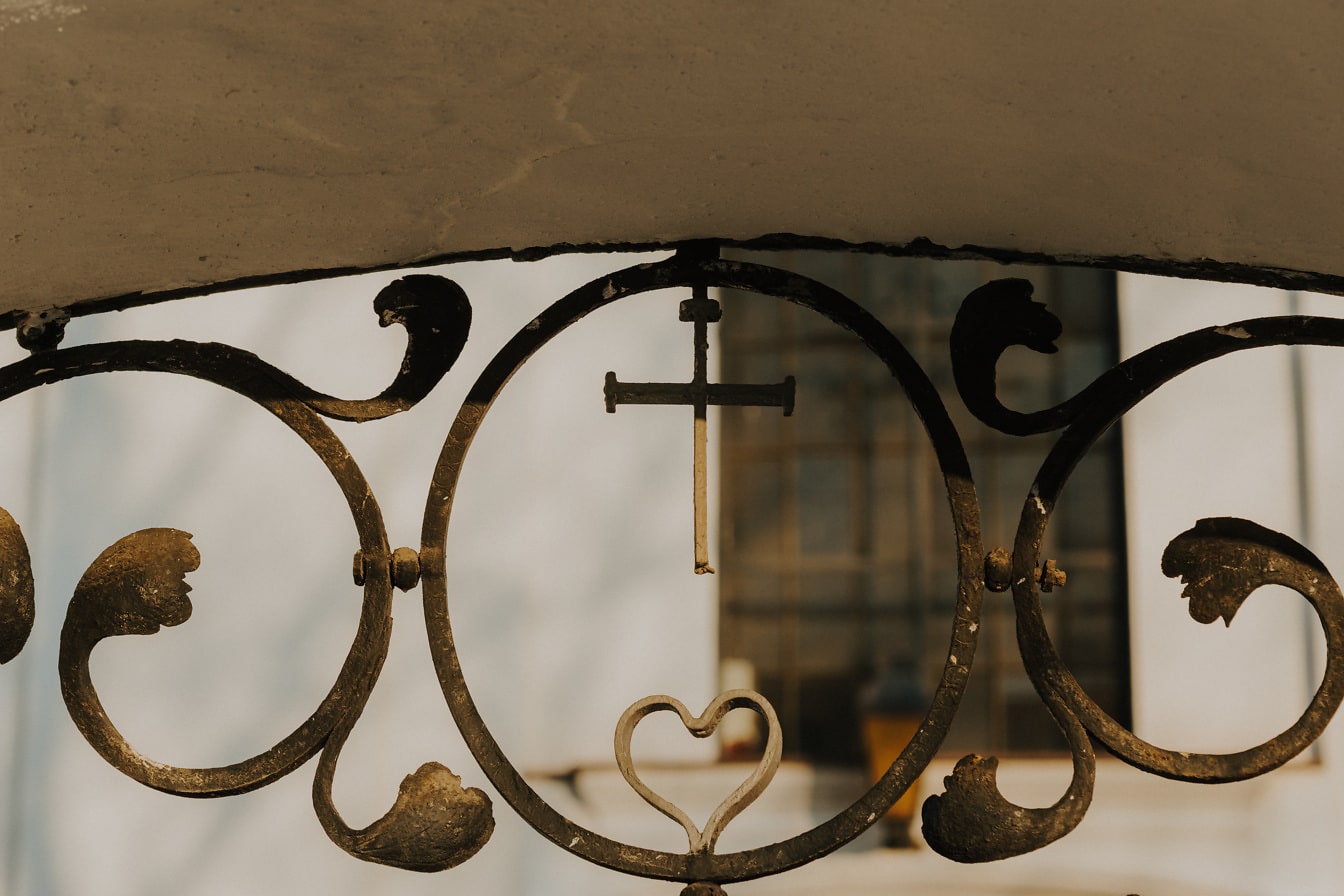 Чугунен кръст със сърце върху ръчно изработена ограда