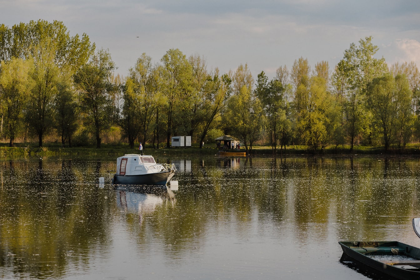 Perahu pesiar putih kecil di tepi danau yang tenang di musim semi
