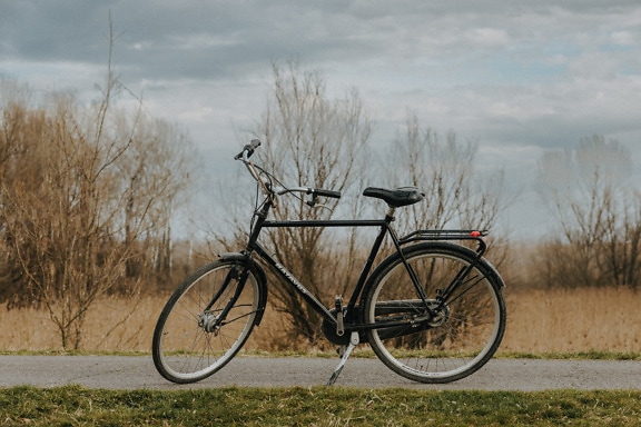 Black classic bicycle parked on asphalt road in countryside