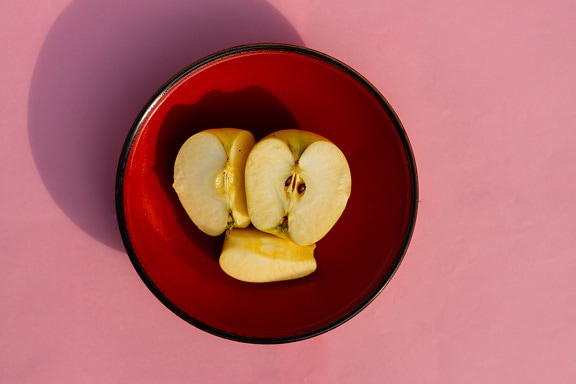 Plátky organického žltého jablka v tmavočervenej miske