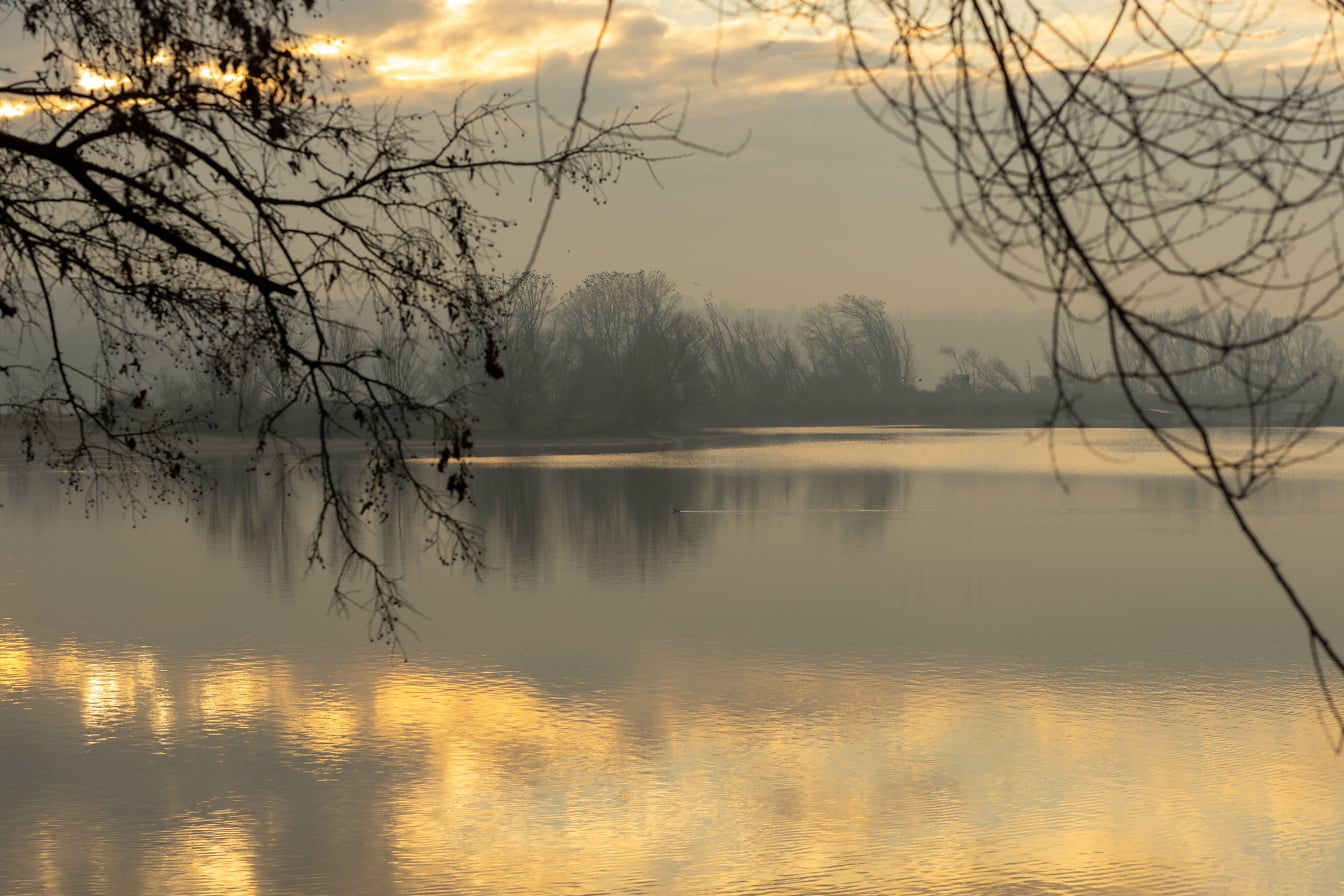 Hmlisté ráno nad pokojným jazerom so zamračenou oblohou