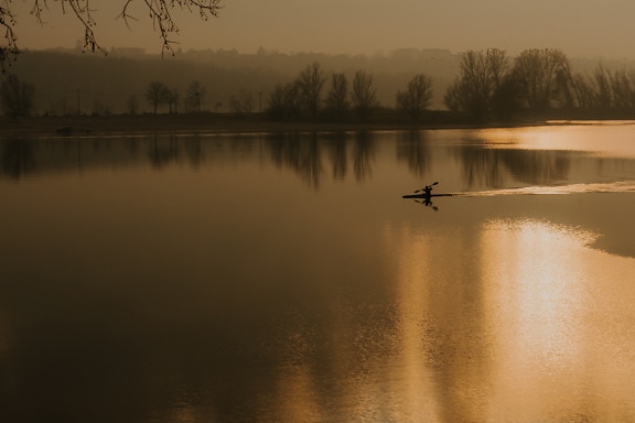 Canoeing on calm lakeside in orange yellow sunset
