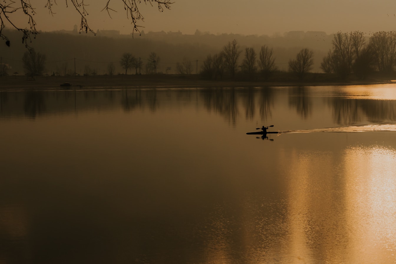 Jazda na kajaku v hmlistom západe slnka na majestátnom brehu jazera