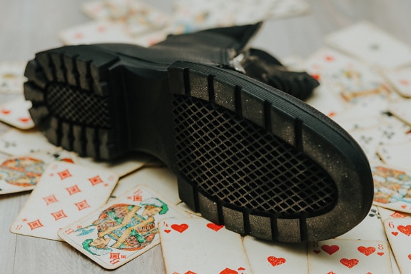 Black rubber sole of a boot on table with playing cards