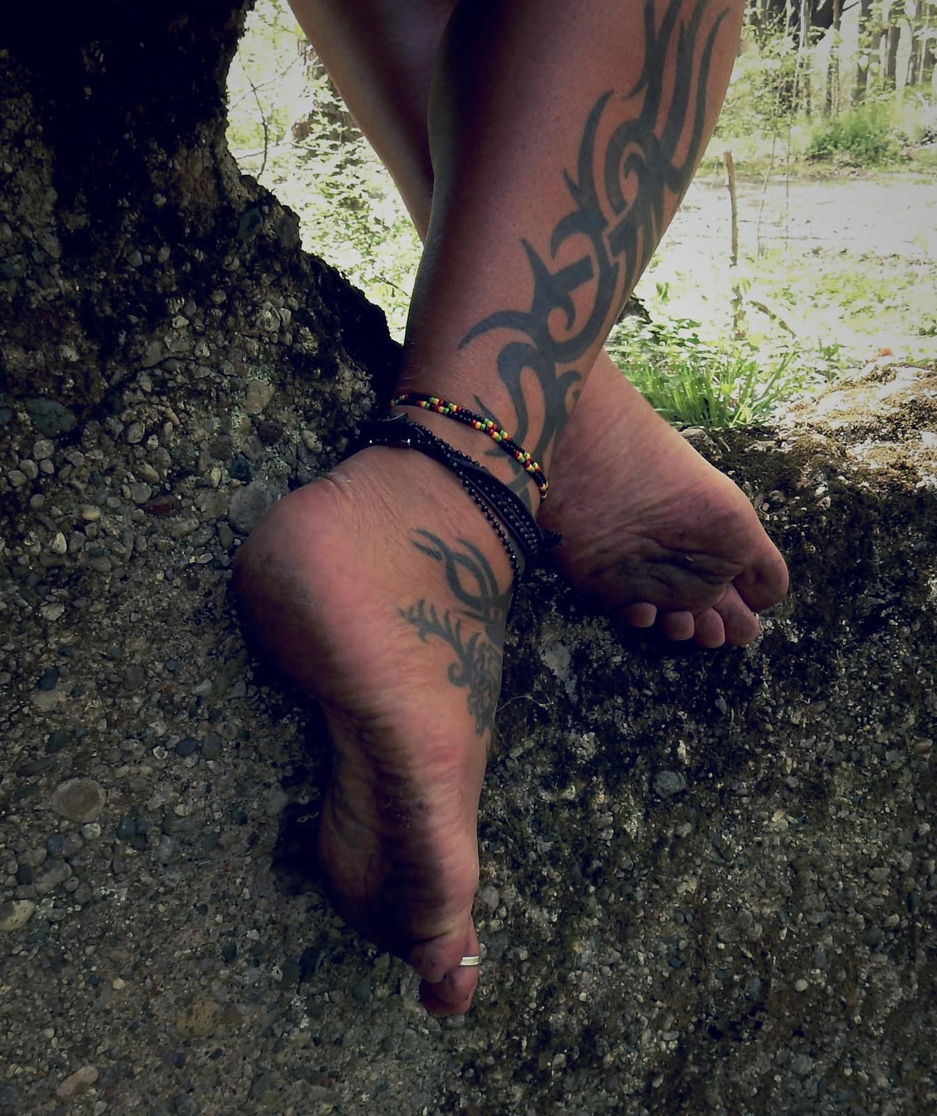 Vuile blote voeten benen met tatoeages en beenarmbanden op oud beton