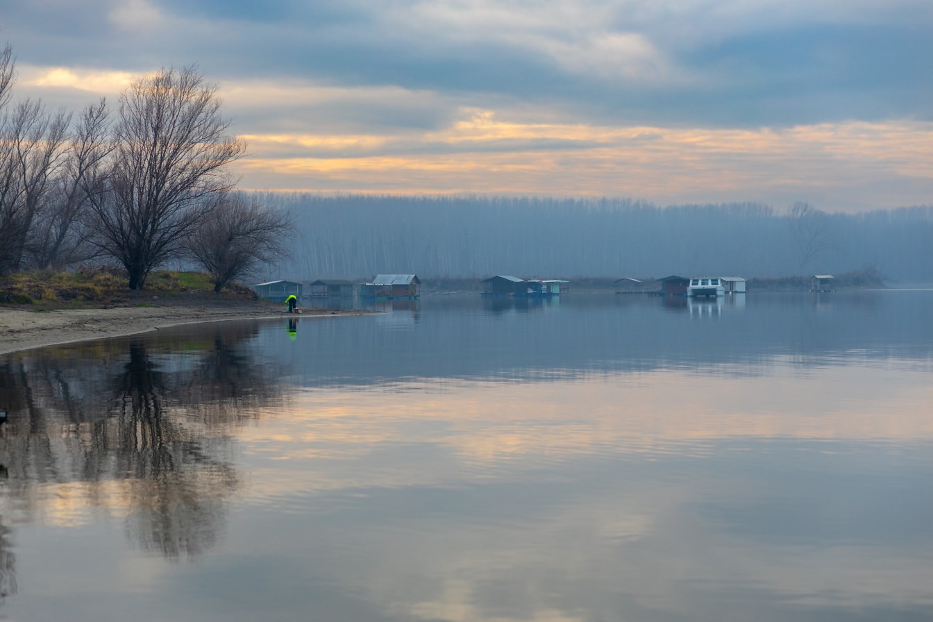 Jezero pejzaž u sumrak s kućicama za čamce
