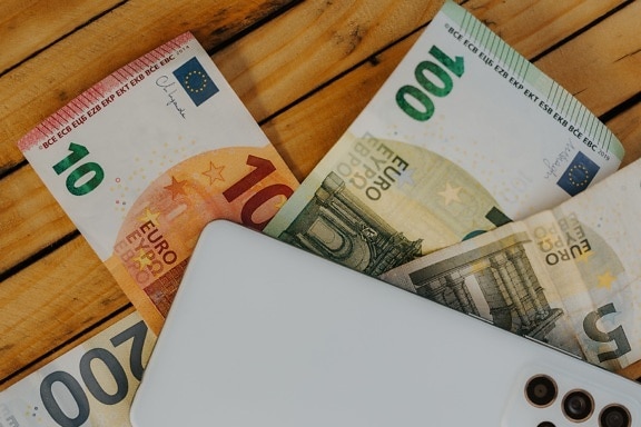 Euro paper money with white cellphone on wooden desk