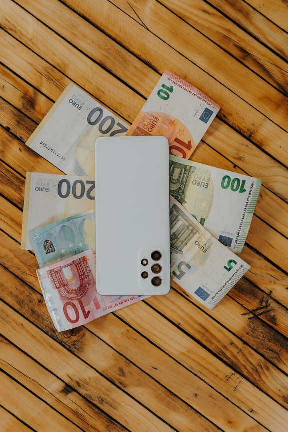 Papierowe pieniądze euro z telefonem komórkowym na jasnobrązowym rustykalnym stole