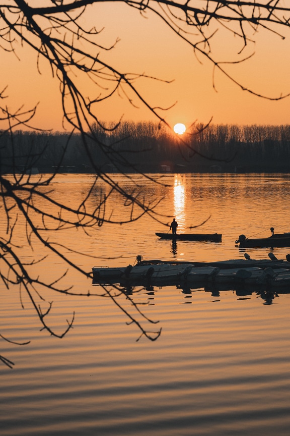 Silhouette of fisherman in fishing boat in sunset in river harbor