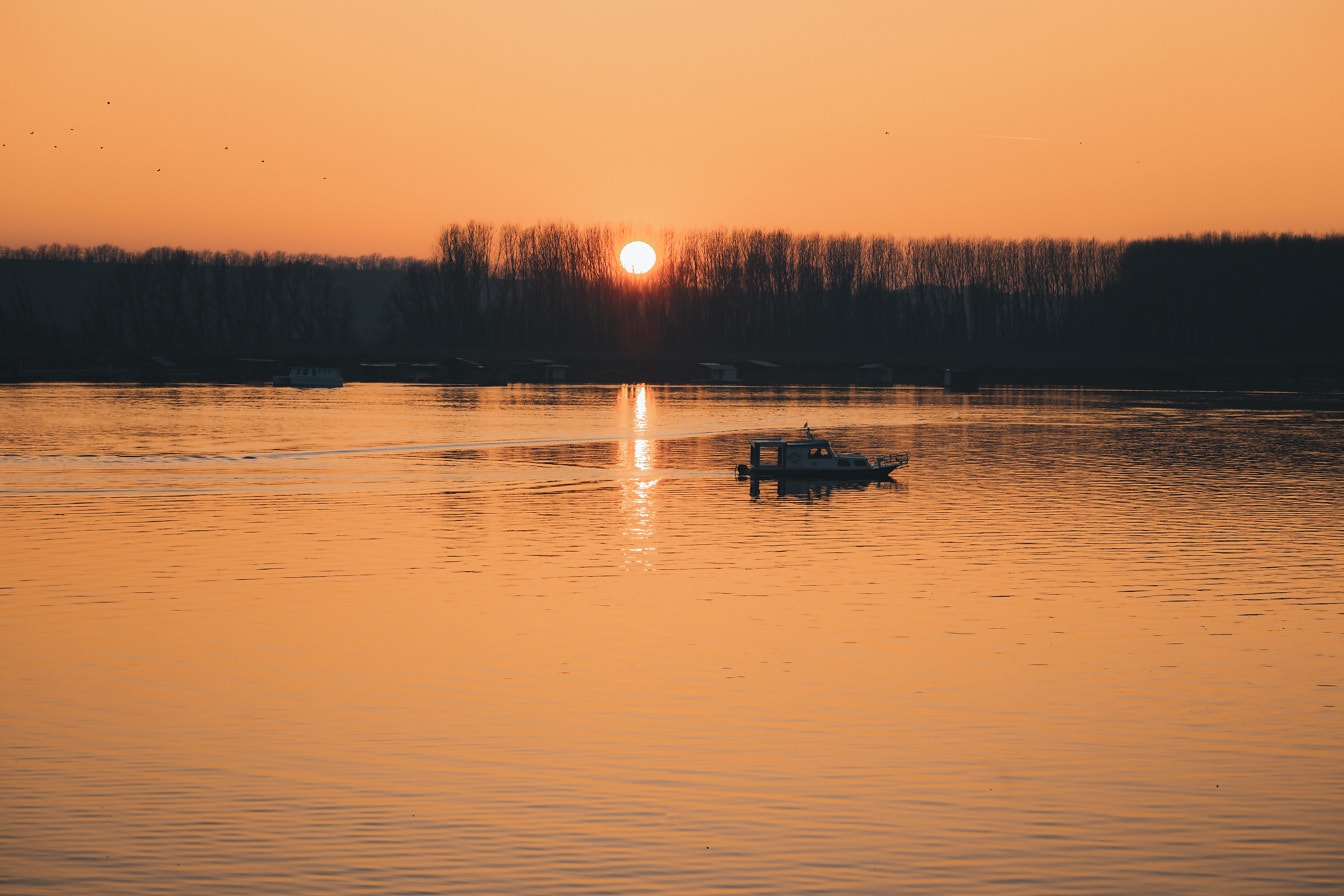 Kis halászhajó jacht naplementekor a nyugodt tóparton