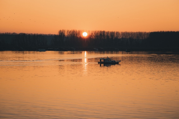 Small fishing boat yacht in sunset at calm lakeside