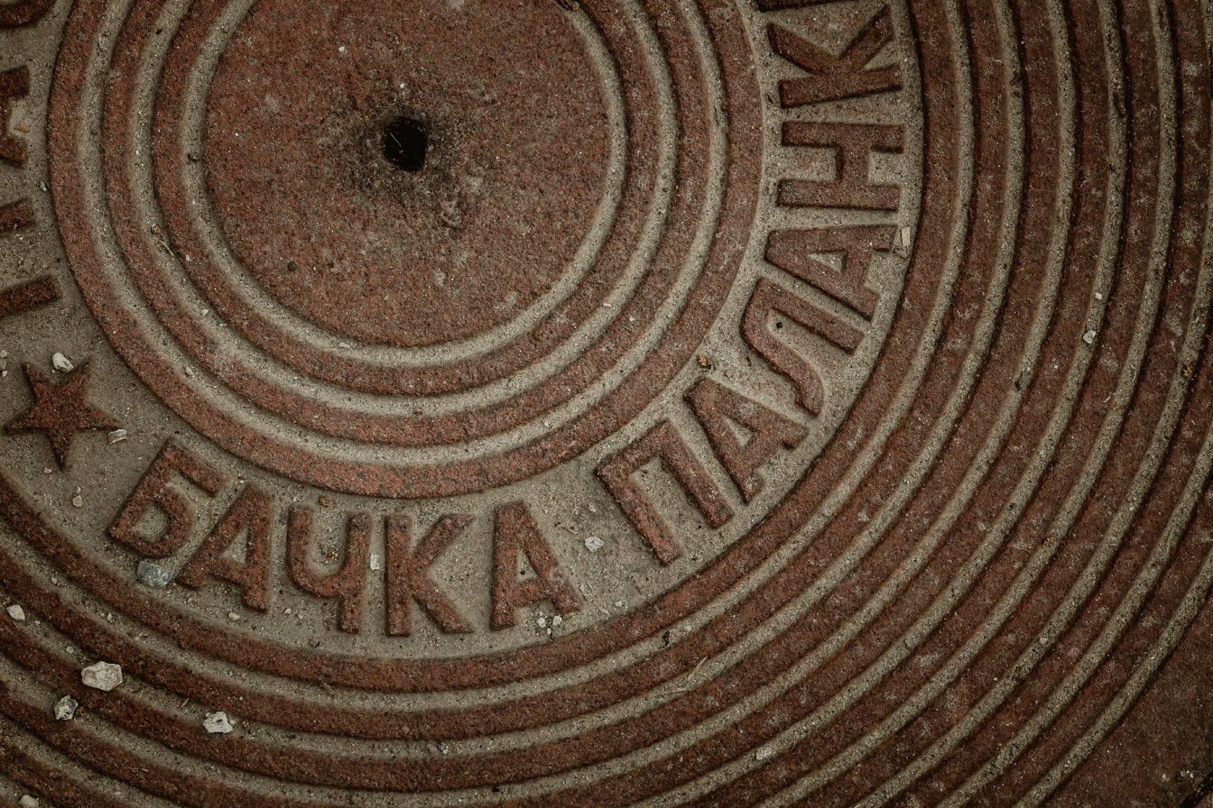 Rust on cast iron manhole cover with cyrillic text texture