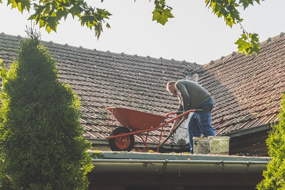 Uomo in piedi sul tetto che pulisce il tetto della casa