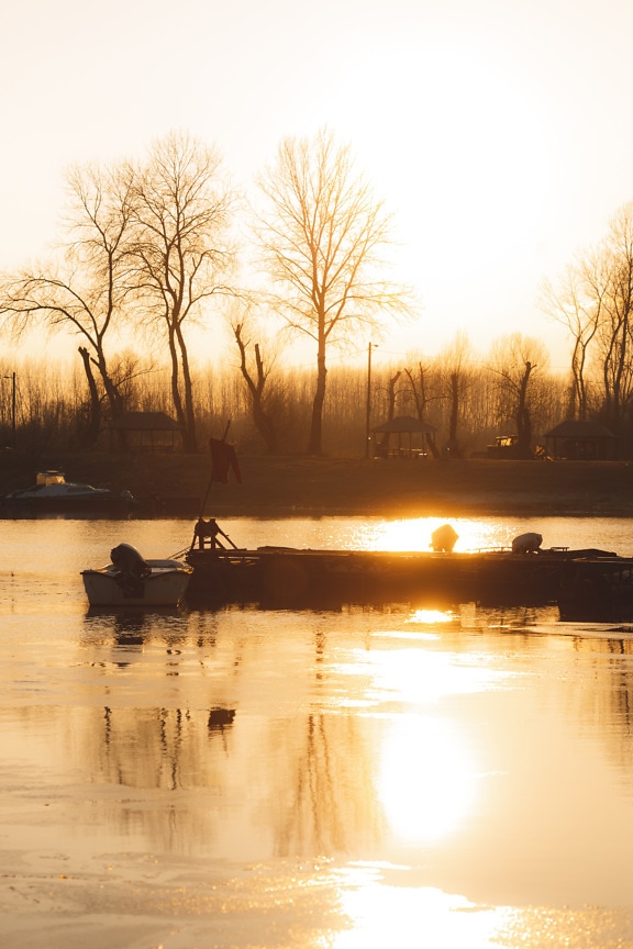 Helle Sonnenstrahlen im Sonnenuntergang am Seeufer mit Silhouette von Booten