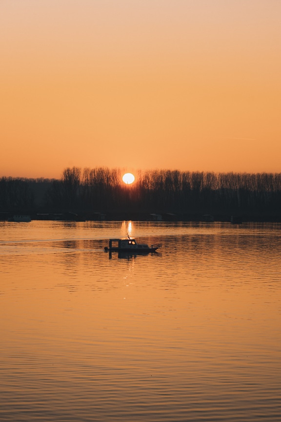 Silhouette of fishing boat in sunset over lakeside